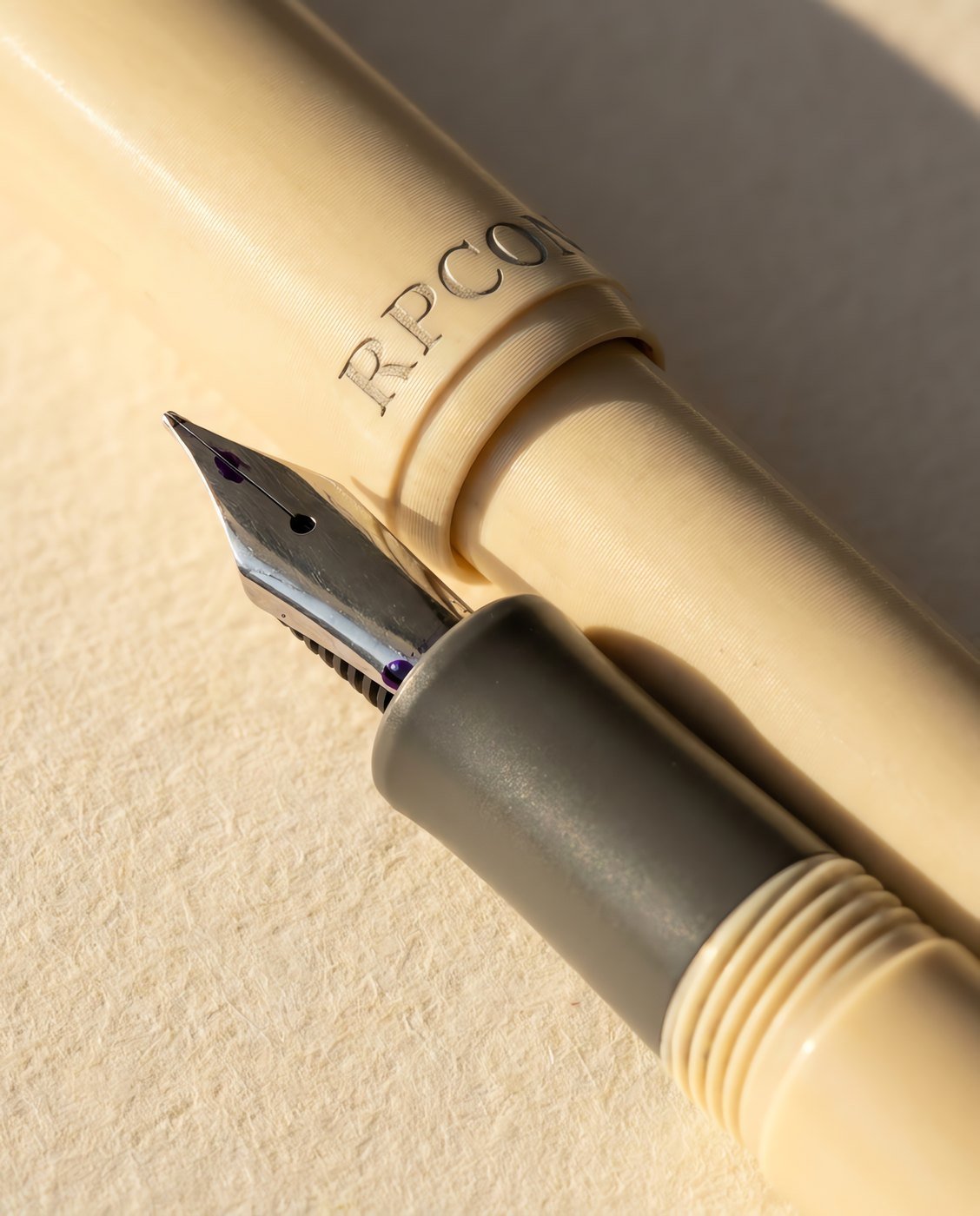 Engrossing No. 6 — A cream acrylic fountain pen with a graphite grey section and a broad stub nib, cap posted in close detail.