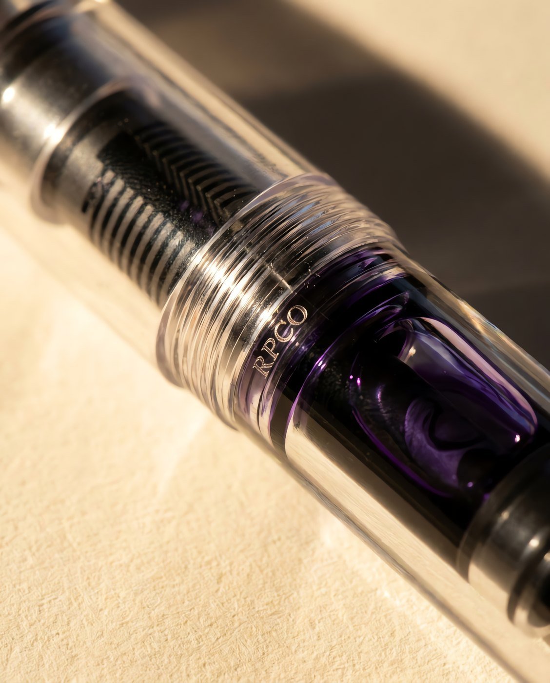 Column Demonstrator — A fully transparent clear acrylic fountain pen showing the dark ebonite feed fins and violet ink inside the converter in close detail.