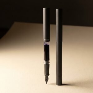 First Entry Pen — A simple charcoal fountain pen with a transparent clear section showing a violet ink cartridge inside.