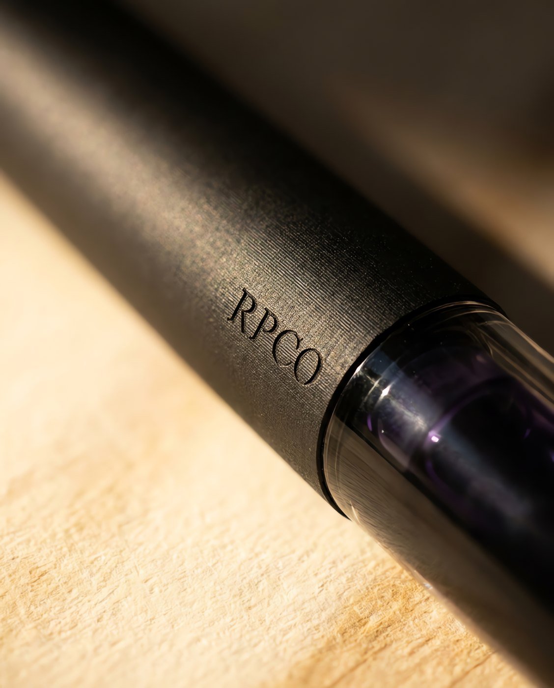 First Entry Pen — A simple charcoal fountain pen with a transparent clear section showing a violet ink cartridge inside in close detail.