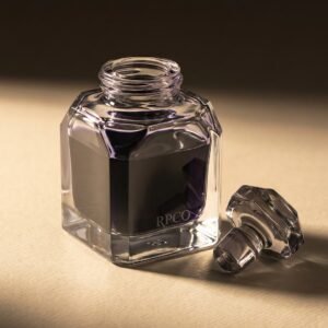Registry Violet, 50 ml — A heavy faceted glass ink bottle three quarters full of dark grey-violet ink with its glass stopper resting beside it.
