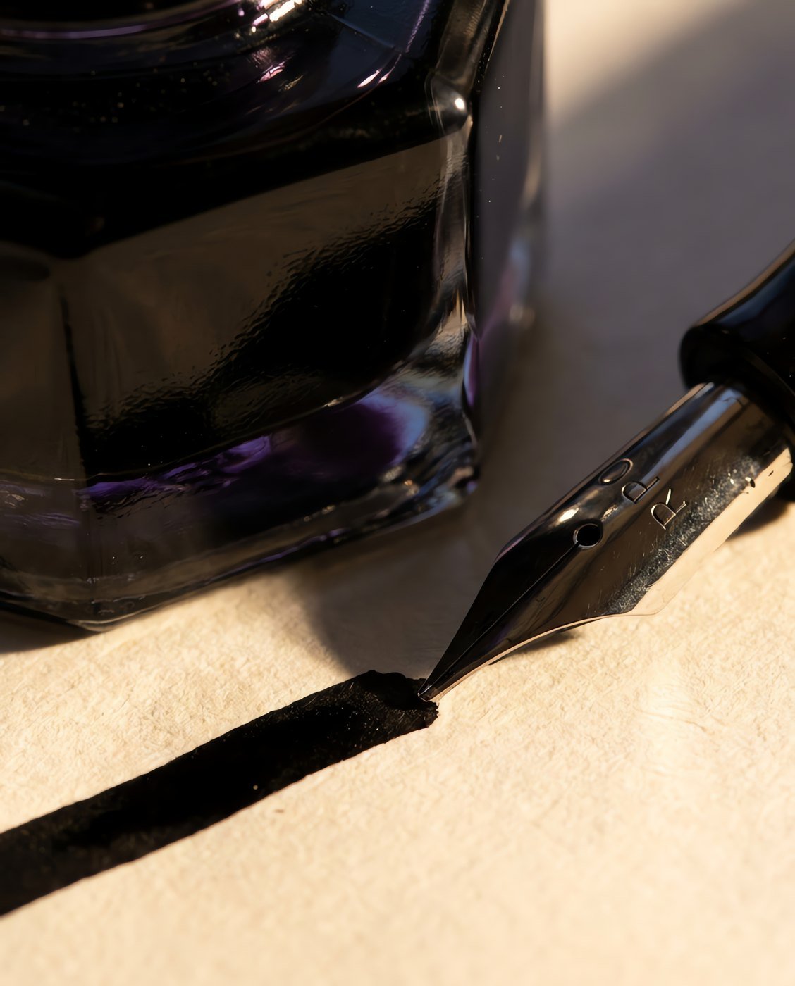 Carbon Black, 50 ml — A faceted glass bottle of dense black ink beside a broad nib laying a flat opaque black stroke on cream paper in close detail.