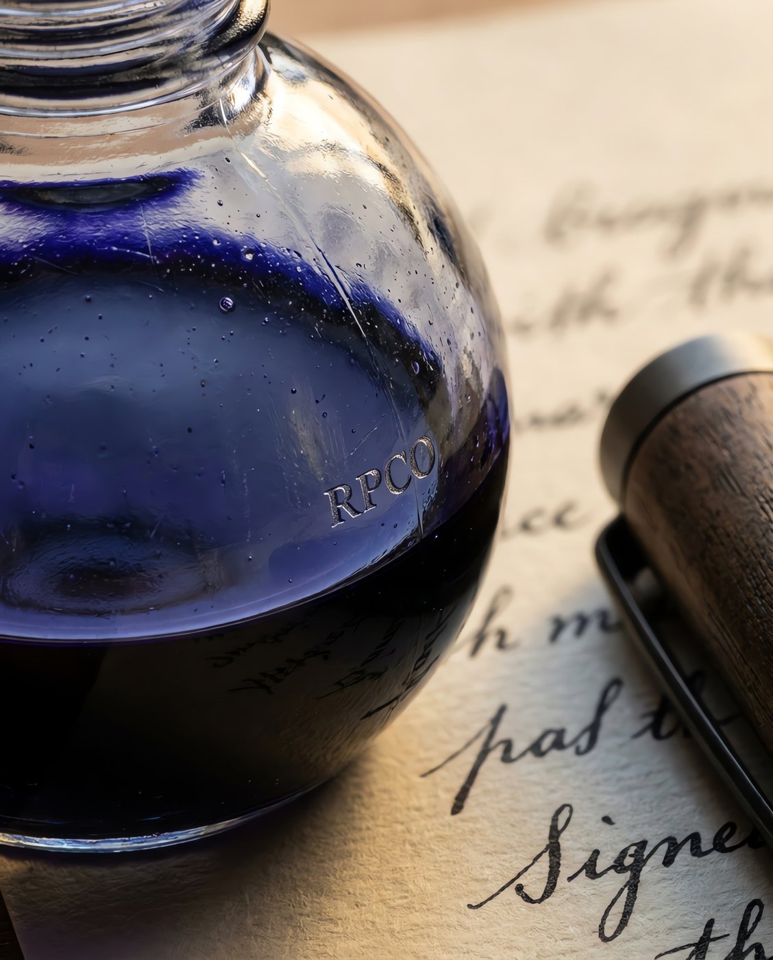 Document Blue, 30 ml — A small round glass bottle of saturated mid-blue ink beside a signed document and a capped pen in close detail.