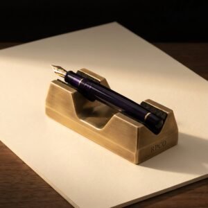 Pen Rest, Machined Brass — A small heavy machined brass pen cradle with two felt-lined vee saddles holding a fountain pen nib-up on a walnut desk.
