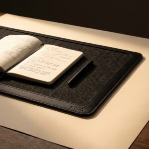 Desk Pad, Leather and Felt — A large charcoal wool felt desk pad with a stitched vegetable-tanned leather edge, an open notebook and a pen lying on it.