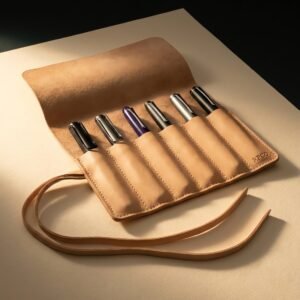 Pen Roll, Six Pen — An undyed vegetable-tanned leather pen roll lying open showing six stitched sleeves holding fountain pens, with a long flat lace tie.