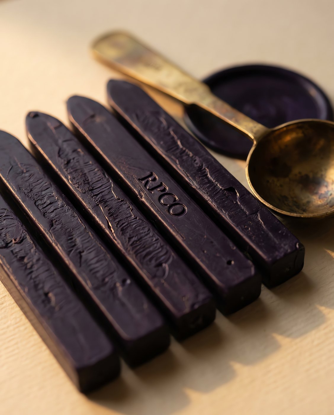 Sealing Wax Sticks, Registry Violet — Five sticks of deep violet sealing wax lying in a row on cream paper beside a brass melting spoon in close detail.