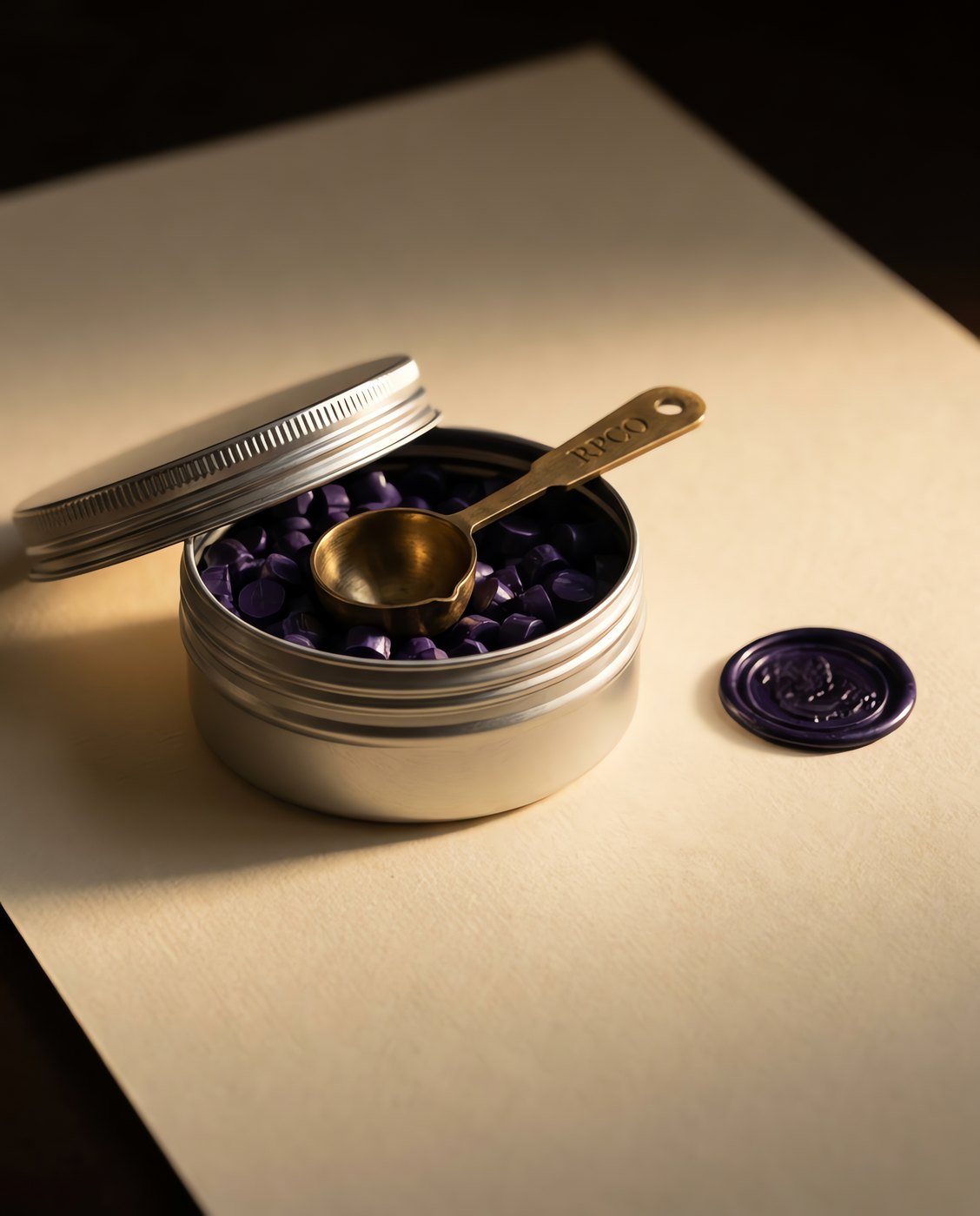 Sealing Wax Beads, Violet, 100 g — An open screw-top tin of small violet wax beads with a small brass measuring scoop, beside a finished wax seal.