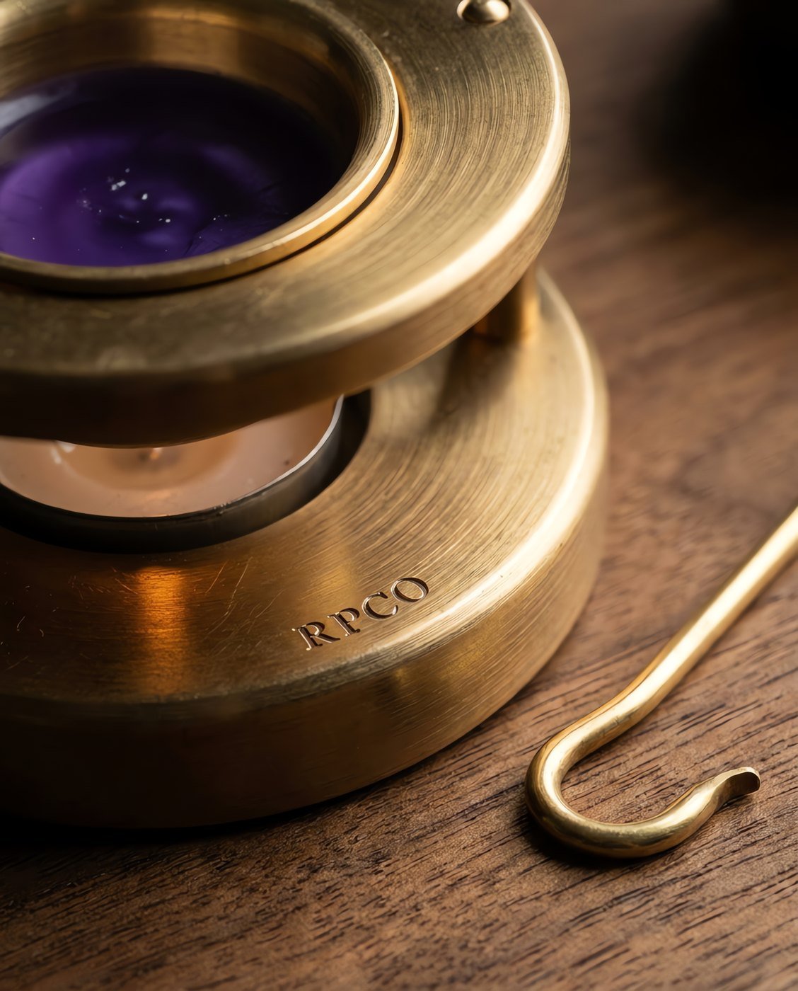 Wax Warmer, Brass — A three-legged spun brass wax warmer with a removable crucible of molten violet wax over a tealight, a hooked lifting tool beside it in close detail.