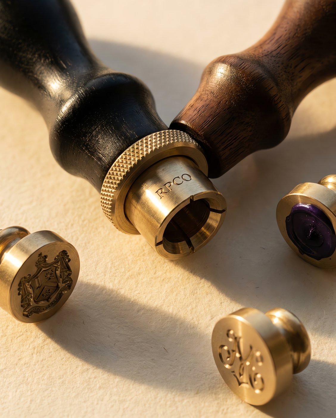 Seal Handle, Walnut — A turned walnut seal handle with a brass collet and knurled locking ring, lying beside three loose engraved brass seal matrices in close detail.