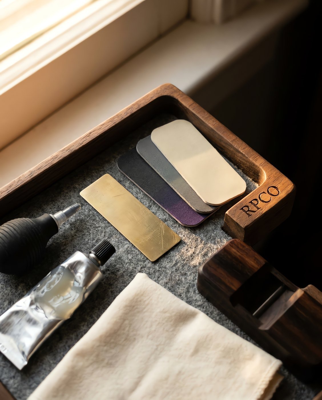 Bench Service Kit — A shallow walnut tray with a felt base holding a brass shim, three sheets of micro-mesh, a bulb syringe, a small tube of grease, a cloth and a hardwood nib block in close detail.